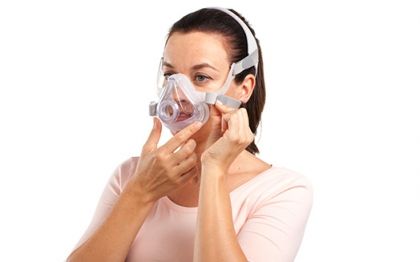 Жена поставя маска за цялото лице ResMed AirFit F10 За Нея 