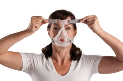 Пациентка със сънна апнея поставя CPAP маска на лицето си. 